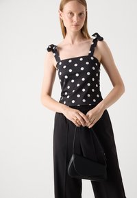 Black polka dot camisole with square neckline and bow detail on straps, paired with black wide-leg trousers and a small black handbag.