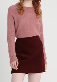 Jasnoróżowy sweter z dzianiny z drobnymi plamkami, w połączeniu z burgundową spódnicą z sztruksu z boczną kieszenią i skośnym wzorem.