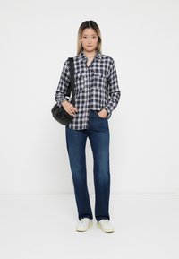Marineblå og hvit rutete flanellskjorte med to brystlommer, kombinert med mørkeblå jeans og hvite sneakers, bærer en svart crossover-veske.