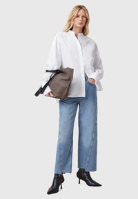 Weißes Langarmhemd mit hohem Kragen, kombiniert mit hellblauen Weitbeinjeans. Dunkelbraune Tasche mit schwarzen Riemen und schwarze Stiefel mit Absatz.