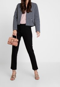 Chaqueta gris corta, top rosa claro, pantalones negros a medida, bolso beige con patrón de cocodrilo y sandalias de tacón alto con estampado de piel de serpiente.