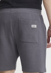 Dark gray shorts made of textured fabric, featuring a back pocket and a small brand label on the pocket. Simple, casual design.