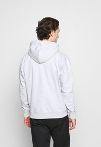 Felpa grigia in cotone con cappuccio regolabile, polsini e vita a coste, texture morbida e vestibilità casual, vista da dietro.