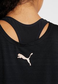 Svart träningslinne med slim fit, i en strukturerad tygkvalitet och med en skuren ryggdesign. Märkbar ljusfärgad Puma-logotyp på nedre vänstra sida.