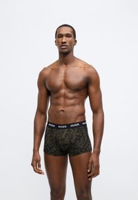 Čierne boxerky s vzorom zlatých listov. Elastický pás s logom "HUGO". Mäkká, elastická látka zdôrazňuje pohodlie a prispôsobenie.