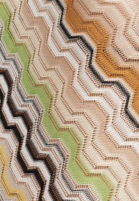 Tela de punto en zigzag con colores alternos en beige, blanco, negro, verde, amarillo y naranja formando un patrón de espiga.