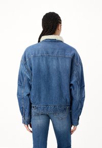 Jeansjacka i blått med en vit, fluffig krage. Löst passform, sänkta axlar och knäppte manschetter. Texturerad denimtyg, inga synliga mönster.