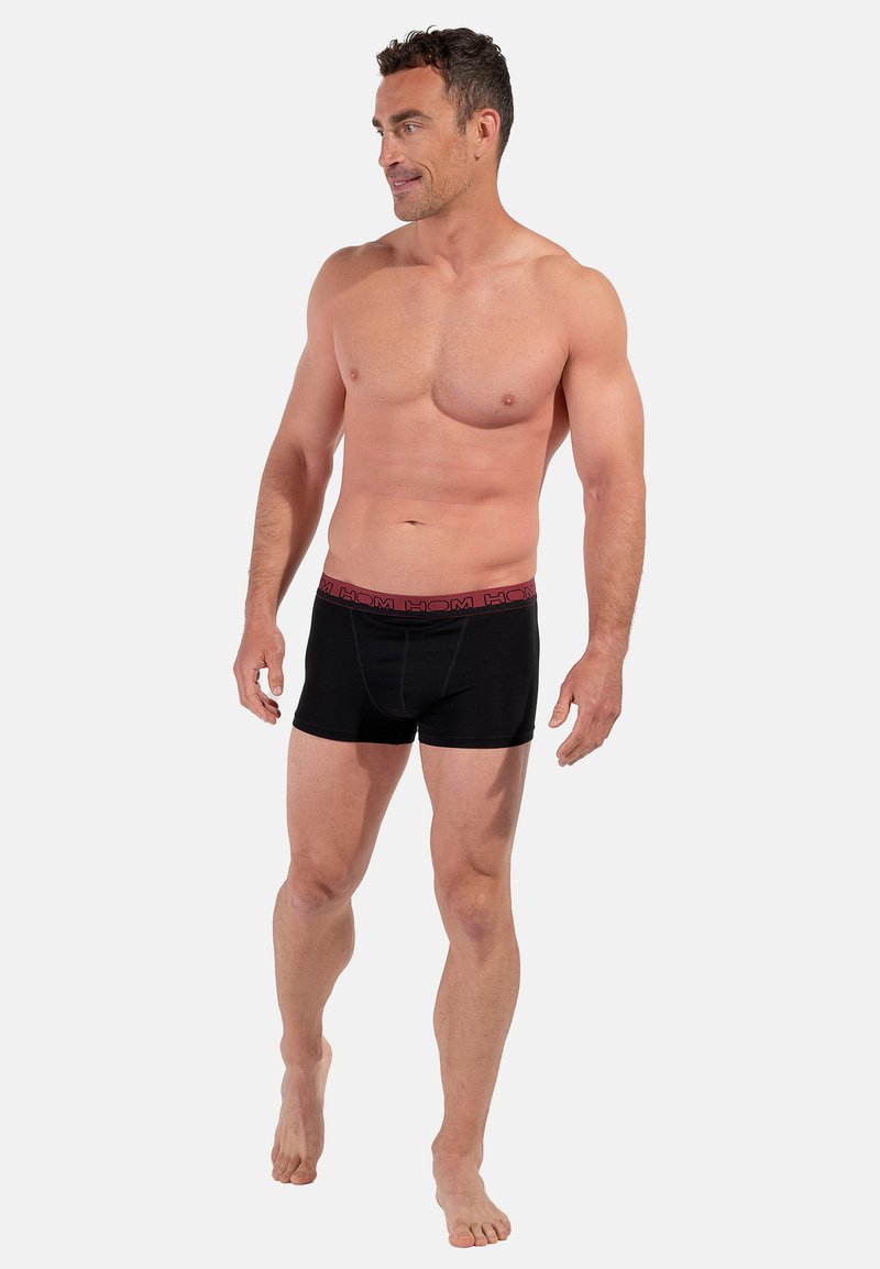 Sorte bokser-shorts med en rød logo på linningen, lavet af et glat, elastisk materiale. Designet har en tætsiddende pasform og kort benlængde.