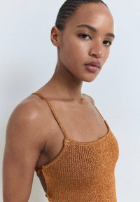 Top in maglia di colore ruggine con spalline sottili e design aderente; presenta una superficie testurizzata e un colletto quadrato.