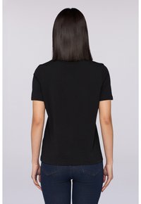 Černé tričko s krátkým rukávem vyrobené z měkké bavlny, s kulatým výstřihem a přiléhavým střihem, nošené s modrými džíny.