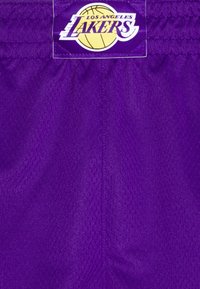 Tejido deportivo púrpura con un parche del logo de Los Angeles Lakers que presenta un balón de baloncesto amarillo y el nombre del equipo.