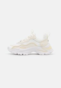Sneaker atletiche con una tomaia in rete bianca, accenti giallo pallido e una suola bianca spessa caratterizzata da un design a onde e modelli testurizzati.