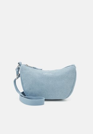 Sac en denim bleu clair à bandoulière avec une texture lisse, fermeture zippée et sangle réglable. Présente un logo prominent sur le devant.