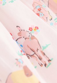Tela rosa claro con un patrón repetitivo de animales de dibujos animados, principalmente vacas, adornadas con flores y acentos de vegetación.