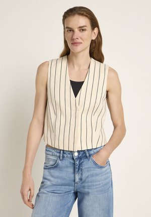 Cropped, sleeveless vest in cream fabric with vertical navy stripes; V-neck design. Paired with light blue, relaxed-fit jeans.