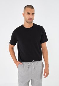 Sort kortærmet t-shirt med rund hals, parret med lysegrå, stribede bukser med snører. Glat stof og løs pasform.