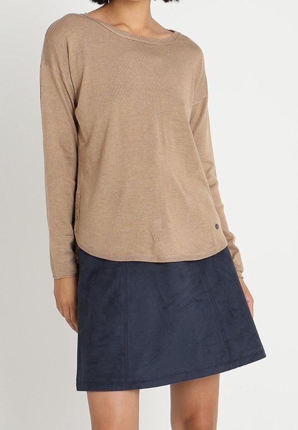 Pull beige à manches longues avec un large col et des boutons sur le côté, associé à une jupe trapèze en daim bleu marine avec des détails de coutures.