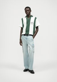 Groen en witte gestreepte polo met korte mouwen, gecombineerd met lichtblauwe cargobroek en zwarte schoenen. Minimalistisch ontwerp met zichtbare stiksels.