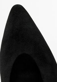 Chaussure en daim noire à bout pointu avec une texture lisse et un détail découpé sur le côté. Des lignes épurées et un design classique mettent en avant l'élégance.