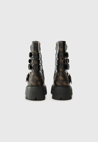 Bottes noires en cuir à la cheville avec des détails brun à motifs, semelle épaisse et fermeture éclair. Elles présentent plusieurs sangles et du matériel en ton doré.