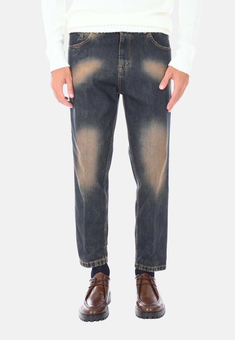 Jeans in denim blu scuro con leggera usura, taglio dritto, hardware in metallo e design classico a cinque tasche, abbinati a scarpe marroni.