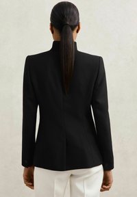 Čierny tailored blazer s textúrovanou tkaninou, so štruktúrovanými ramenami a priliehavým strihom. Dlhé rukávy s gombíkovými akcentmi.