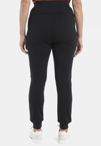 Pantaloni da jogging neri con vita elasticizzata e polsini aderenti. Realizzati in materiale morbido ed elastico. Calzature caratterizzate da sneaker bianche con suole testurizzate.