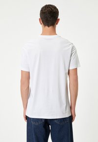 Hvid bomulds t-shirt med korte ærmer, rund hals og en afslappet pasform, parret med mørkeblå, løstsiddende jeans. Ingen synlige mønstre.
