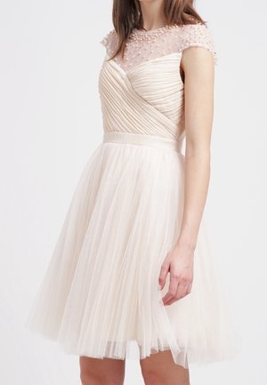 Sleeveless ivory dress with a fitted bodice, pleated skirt, and sheer, beaded overlay. Textured fabric with subtle shimmer and volume.