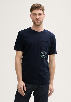 Navy blue short-sleeve t-shirt made of cotton. Features a chest pocket with white text and graphics. Smooth texture and relaxed fit.