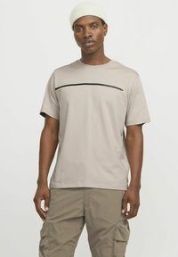 Camiseta corta de manga corta en color beige claro, hecha de algodón y con un cuello redondo. Presenta una línea negra horizontal en el pecho.