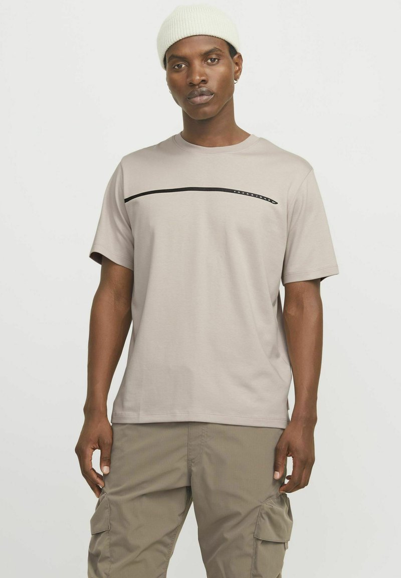 Camiseta corta de manga corta en color beige claro, hecha de algodón y con un cuello redondo. Presenta una línea negra horizontal en el pecho.