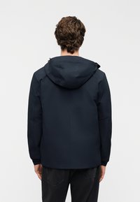 Ναυτικό αδιάβροχο μπουφάν με κουκούλα, με λεία υφή, ίσια κοπή και ρυθμιζόμενα κορδόνια στη λαιμόκοψη και τα μανίκια.