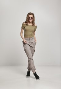 Top de color verde oliva, sin mangas y con un diseño ajustado, combinado con pantalones cargo beige claro que cuentan con puños elásticos y múltiples bolsillos. Zapatillas negras.