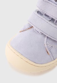 Ελαφρύ παπούτσι σουέντ σε χρώμα λεβάντας με δύο λουράκια βέλκρο, στρογγυλεμένη λαστιχένια σόλα και ραφές κοντά στη μύτη και τα λουράκια.