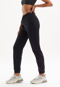 Zwarte sweatpants met een elastische tailleband en zijzakken, taps toelopende enkels, gecombineerd met grijze en witte sneakers met textuuraccenten.