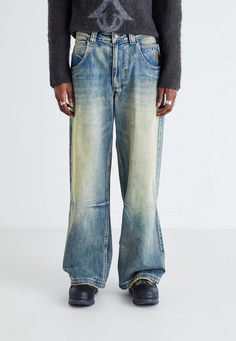 Wide-leg denim jeans in a faded blue wash, featuring copper hardware, five pockets, and subtle stitching details on the front.