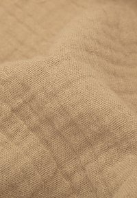 Beżowa tkanina o teksturowanym, tkanym wyglądzie; posiada wzór w kratkę; miękka i lekka, o naturalnym, ziemistym odcieniu.