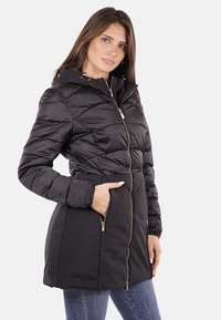 Giacca a vento nera con zip frontale, cappuccio e due tasche con cerniera. Presenta un motivo trapuntato, una texture liscia e dettagli in metallo color oro.