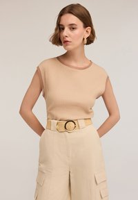 Beige ribbed sleeveless top with a contrasting brown neckline, paired with high-waisted beige cargo pants and a woven belt with a round buckle.