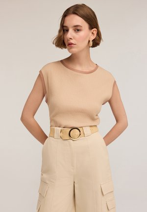 Top bej cu dungi, fără mâneci, având un guler maro în contrast, asortat cu pantaloni cargo bej cu talie înaltă și o curea împletită cu o cataramă rotundă.