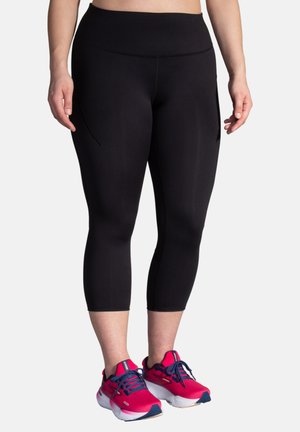 Zwarte capri leggings met een zachte textuur en hoge taille, voorzien van zijzakken en gedragen met roze sport schoenen.