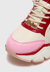 Zapatilla chunky con una mezcla de materiales rojos brillantes, rosa suave y crema. Presenta herrajes dorados y acentos texturizados en la parte superior.