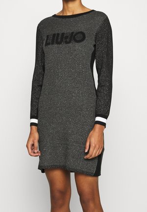 Woman wearing a black and silver long-sleeve knitted mini dress with textured fabric and subtle sparkle details.