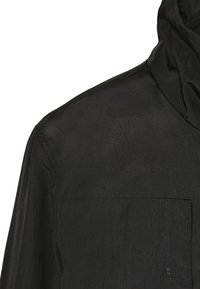Camisa de tela ligera y negra con cuello alto, un bolsillo en el pecho y textura suave; presenta líneas limpias y un diseño minimalista.