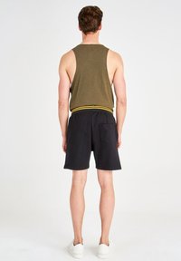 Débardeur vert avec une ceinture jaune accentuée, associé à un short noir. Le mannequin présente la vue de dos, mettant en valeur le design et la coupe décontractés.