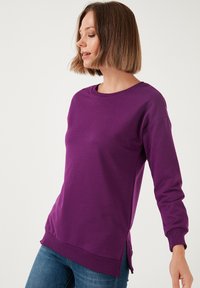 Felpa viola con scollatura tonda, maniche lunghe, polsini a coste e spacchi laterali all'orlo, realizzata in un tessuto morbido e confortevole.