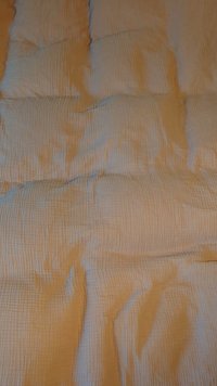 Quilted blanket with a textured surface, featuring a soft, cream-colored fabric and subtle vertical patterning throughout.