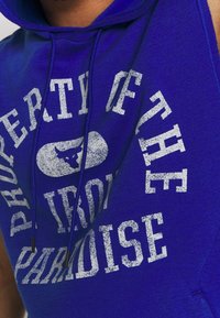 Felpa senza maniche blu con grafica frontale in testo bianco che recita "PROPRIETÀ DELL'IRON PARADISE" con un design testurizzato.