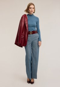 Geribbelde blauwe coltrui, op maat gemaakte grijze broek, bordeaux faux leren jas over de schouder, goud-accentueerde riem, kastanjebruine hakken.